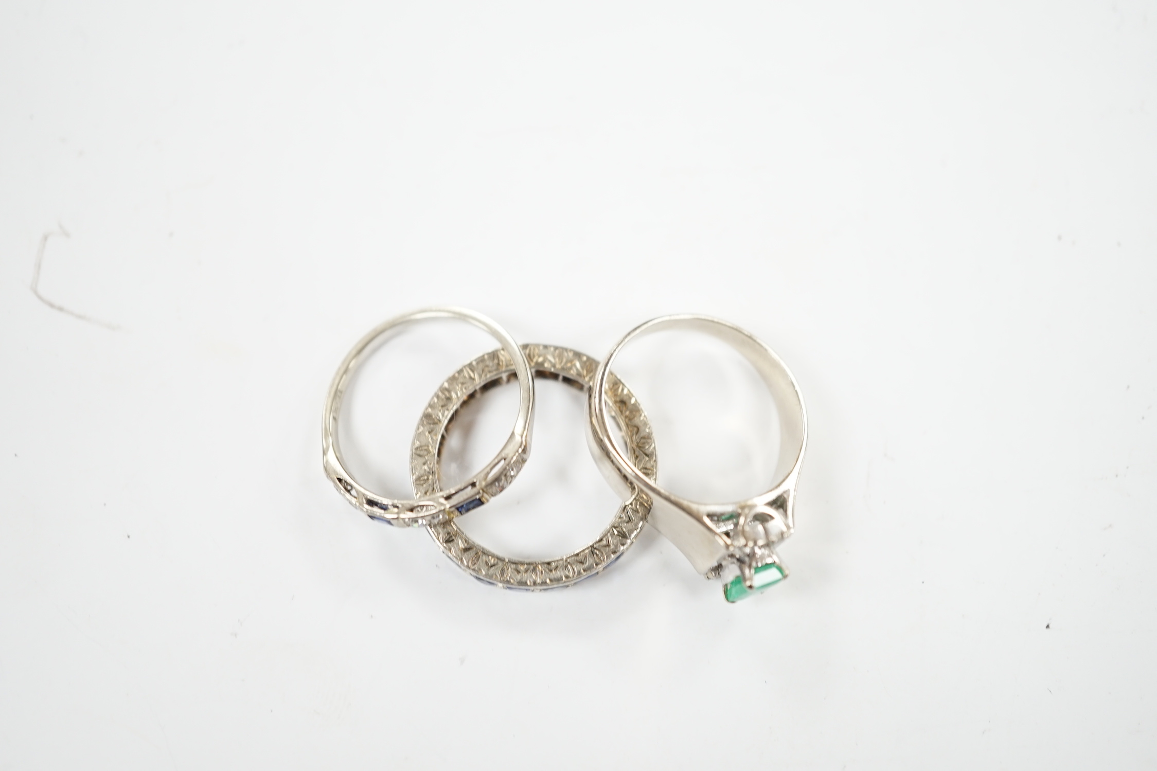 An 18k white metal, emerald and diamond set dress ring, size O, a white metal and sapphire set full eternity ring (stones missing) and an 18ct, sapphire and diamond set half hoop ring, gross weight 10 grams.